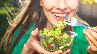 mulher a comer salada de uma taça